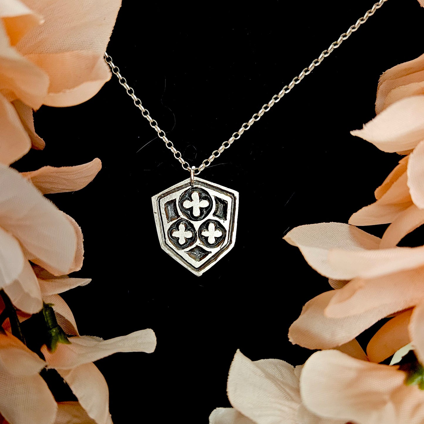 Silver necklace with a shield-shaped pendant on a black background with pink flowers