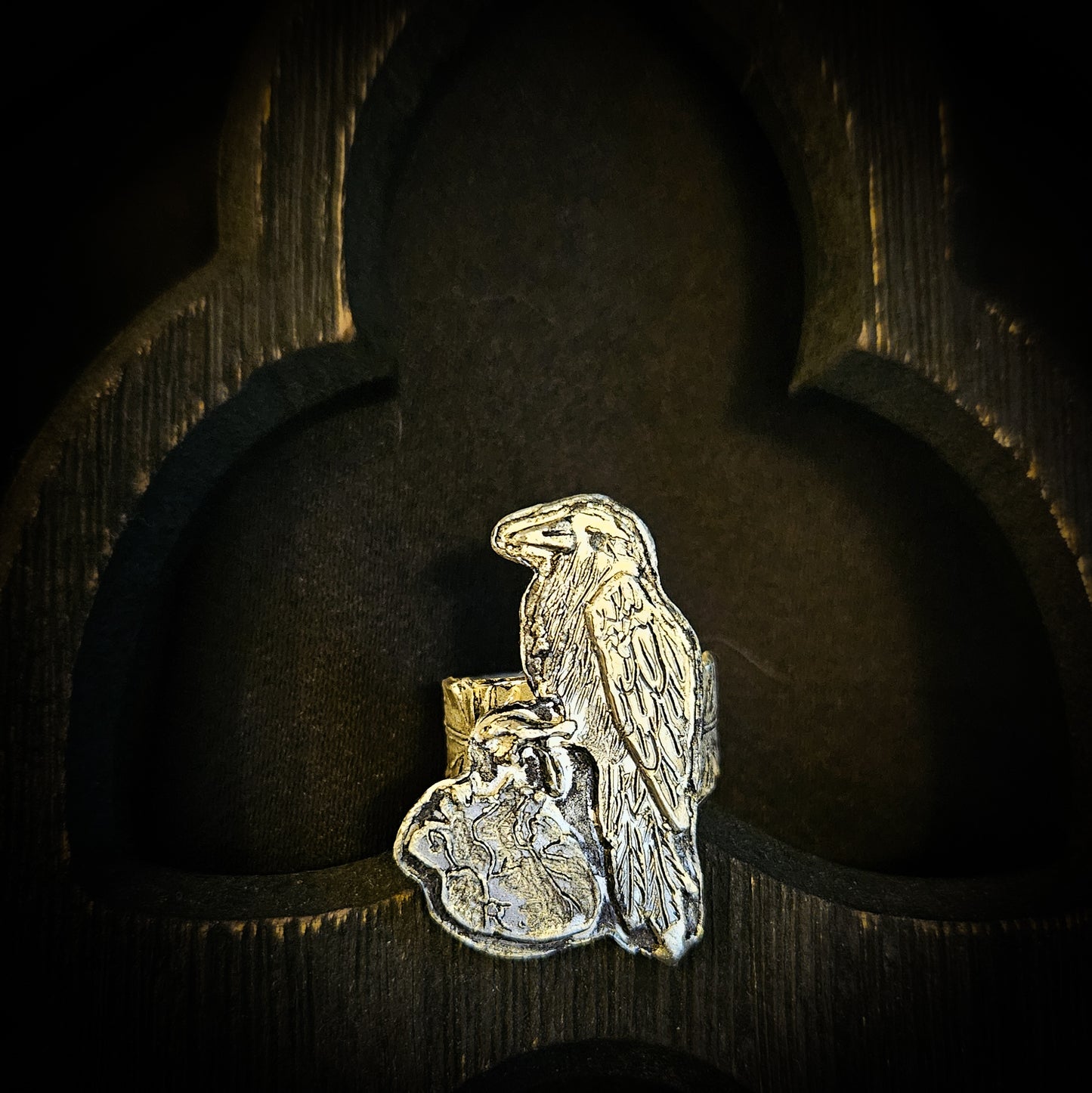 Sterling silver raven and human heart ring with a feather band on a dark wood background