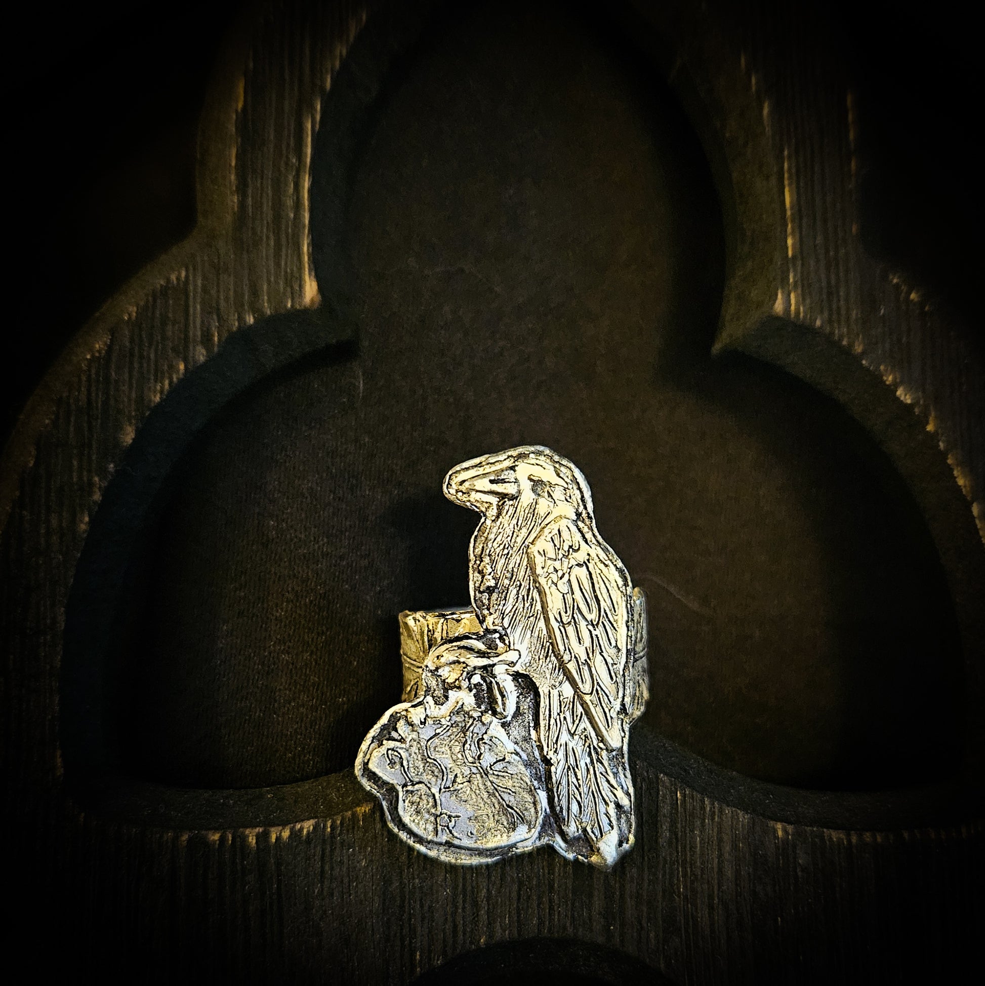 Sterling silver raven and human heart ring with a feather band on a dark wood background