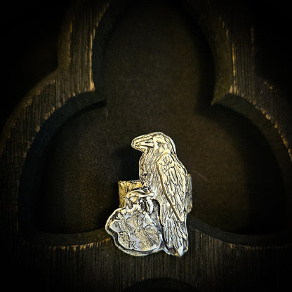 Sterling silver raven and human heart ring with a feather band on a dark wood background
