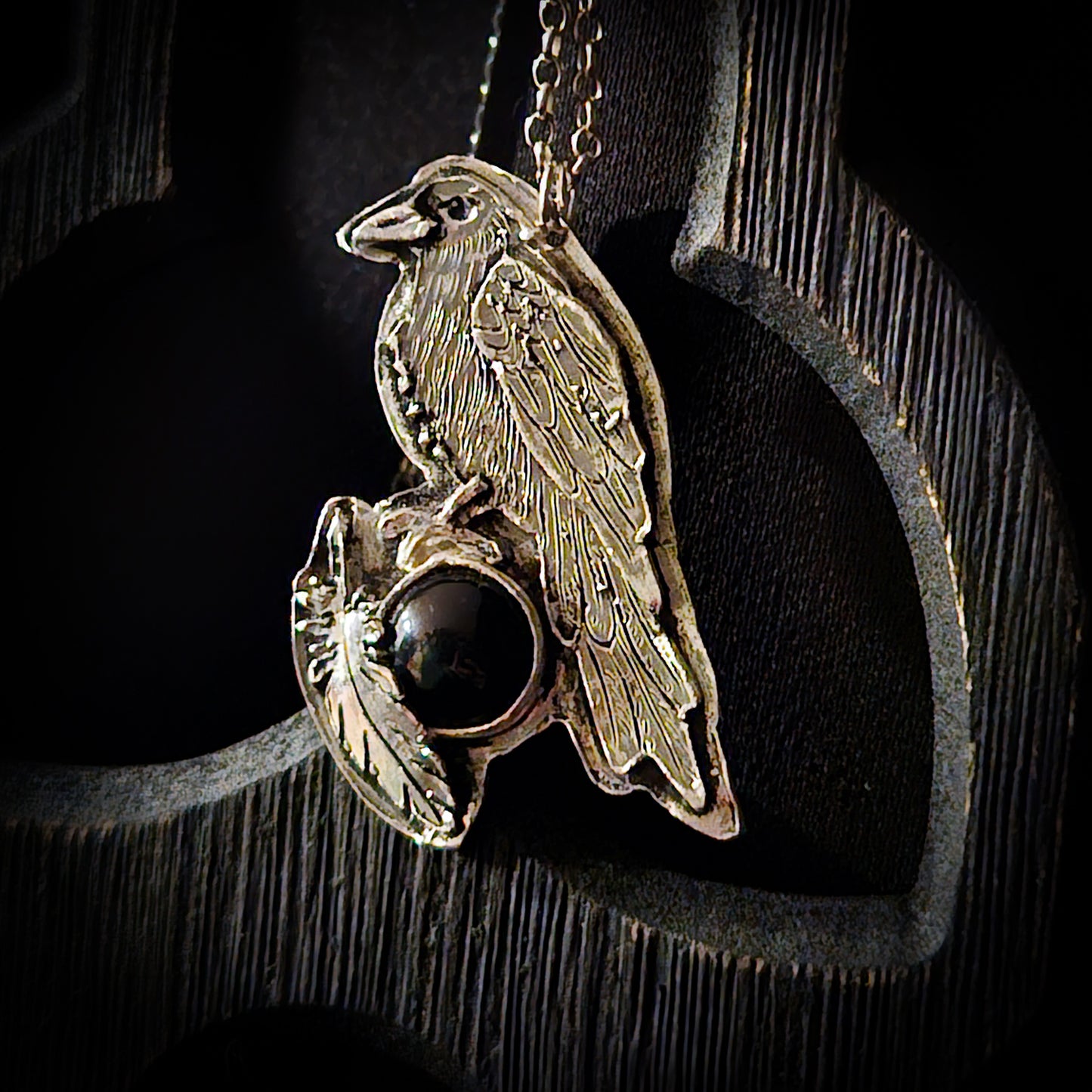 Sterling silver bird pendant with black stone on a chain against a dark wooden background