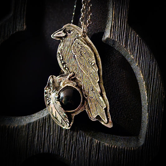 Sterling silver bird pendant with black stone on a chain against a dark wooden background