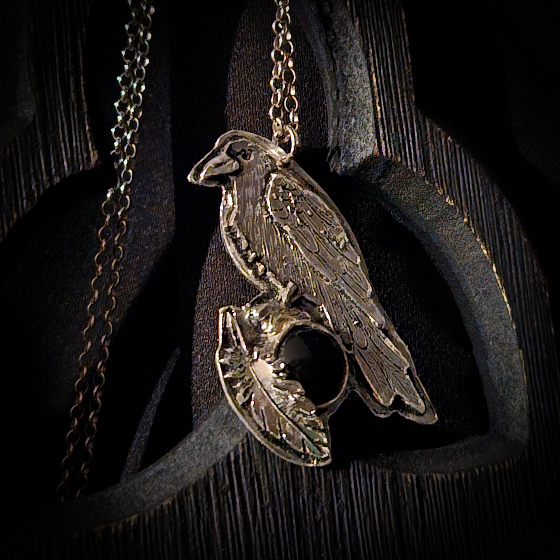Sterling silver bird pendant with black stone on a chain against a dark wooden background