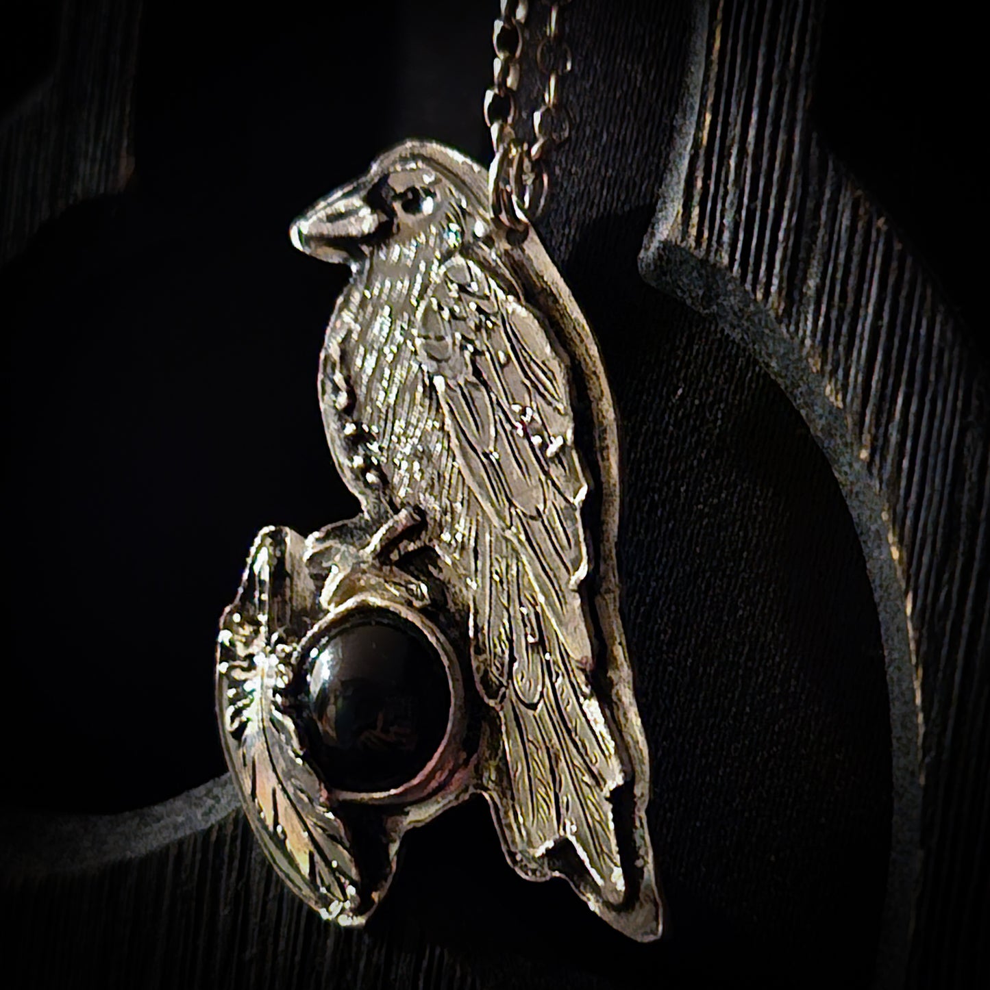 Silver pendant with a bird design and dark gemstone on a black background