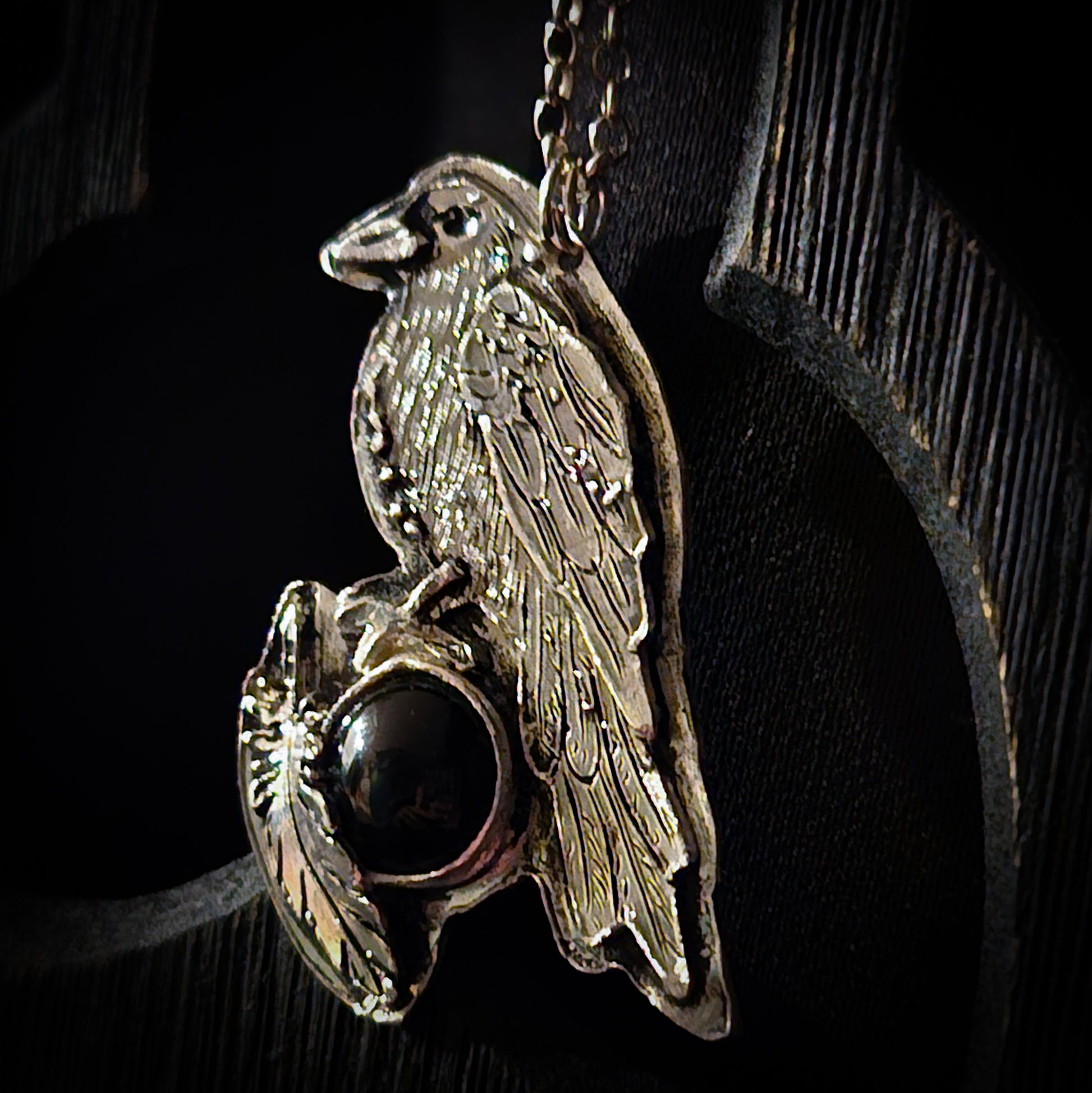 Silver pendant with a bird design and dark gemstone on a black background