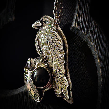 Silver pendant with a bird design and dark gemstone on a black background