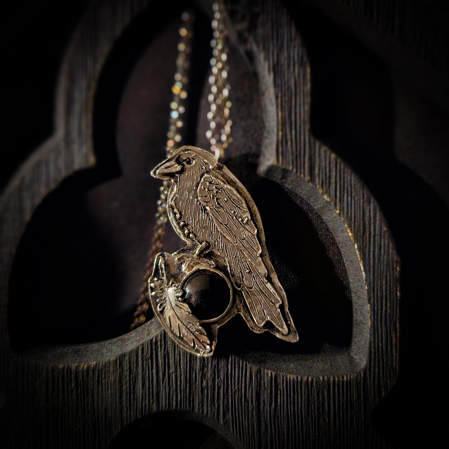 Silver pendant with a bird design and dark gemstone on a black background