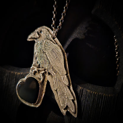 Sterling silver bird pendant with black heart stone on a chain against a dark wooden background