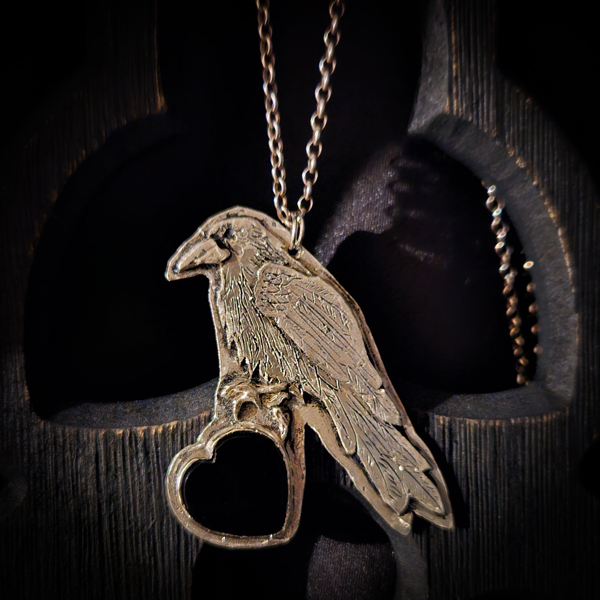 Sterling silver bird pendant with black heart stone on a chain against a dark wooden background