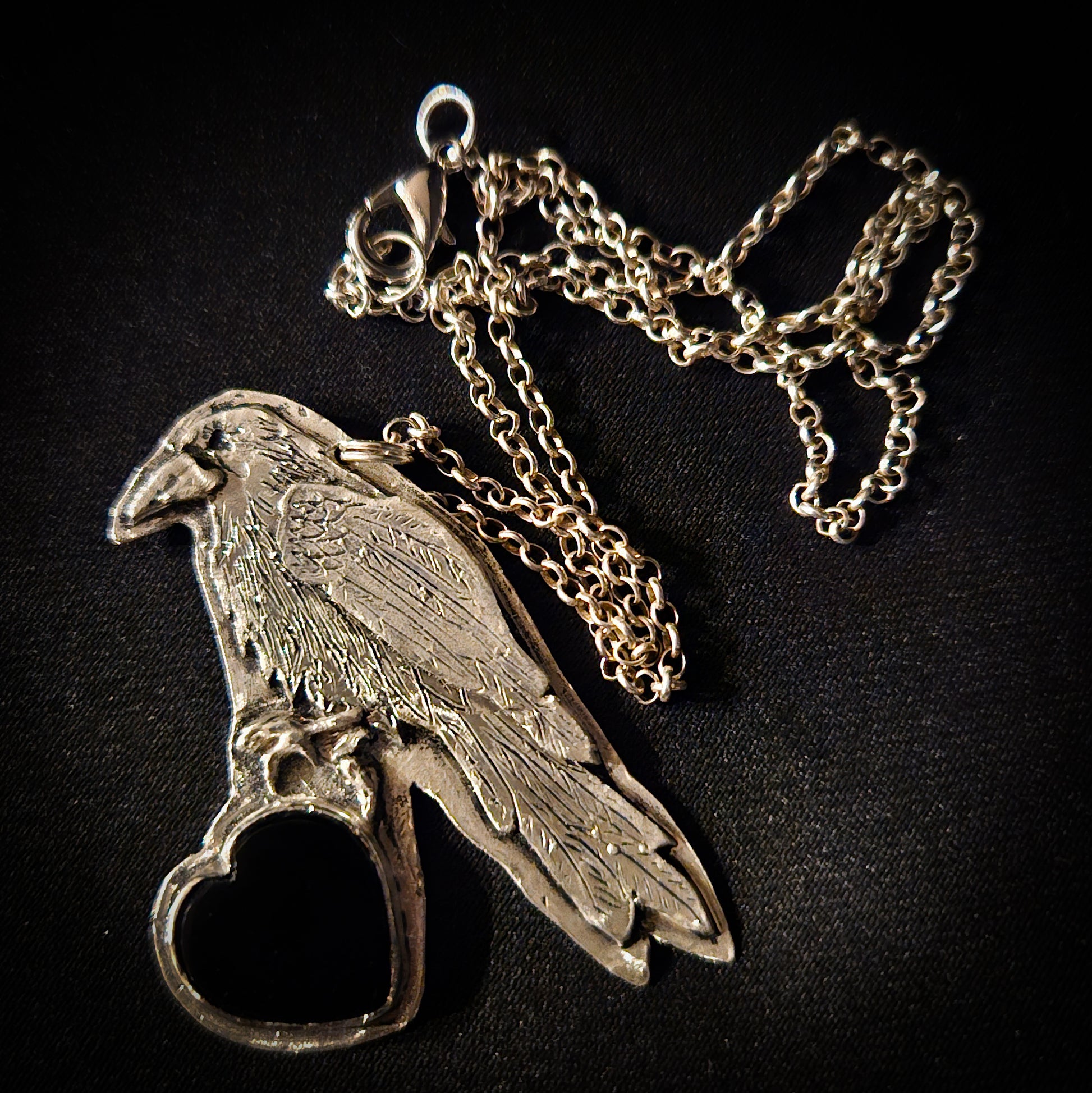 Sterling silver bird pendant with black heart stone on a chain against a dark wooden background
