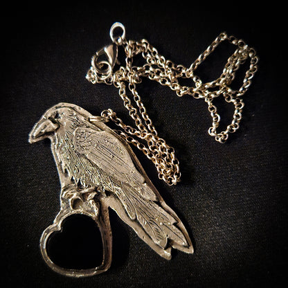 Sterling silver bird pendant with black heart stone on a chain against a dark wooden background