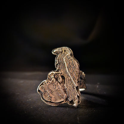 Sterling silver raven and human heart ring on a dark background