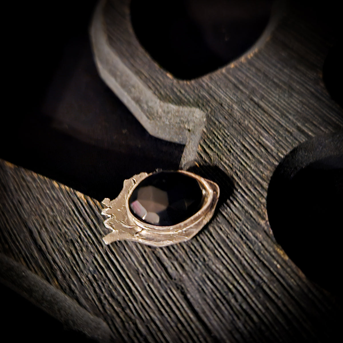 Silver ring with a black stone set on a heart shaped base displayed a wooden surface