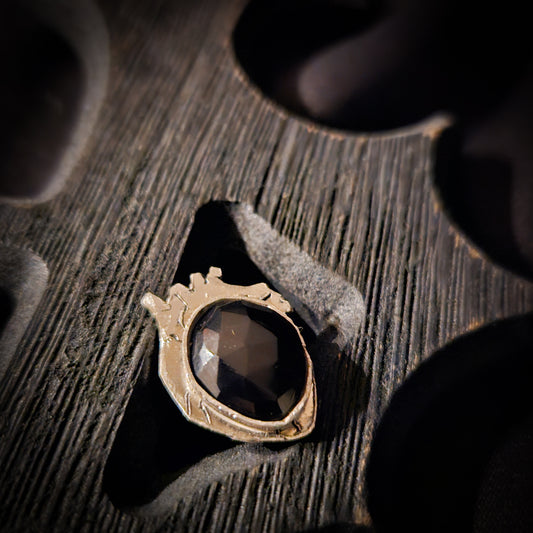 Silver ring with a black stone set on a heart shaped base displayed a wooden surface