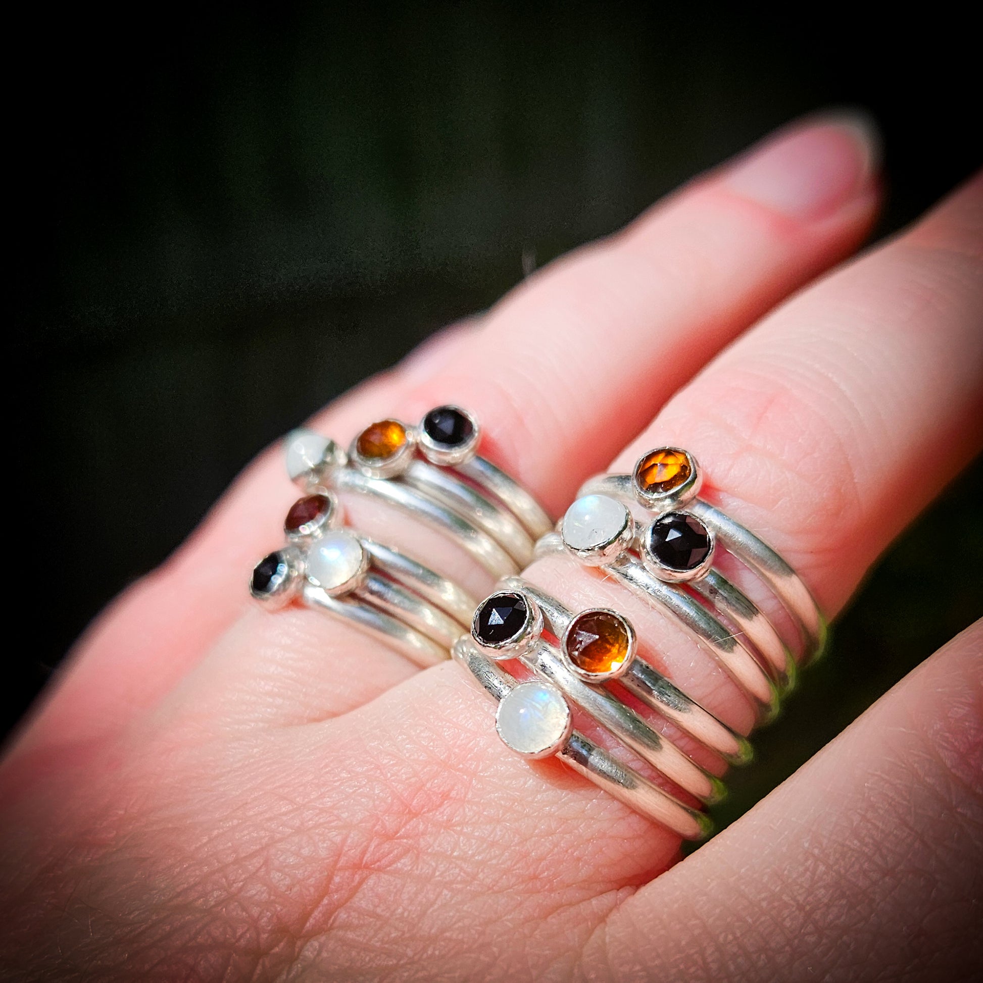 Silver rings with multicolored gemstones on a hand against a dark background