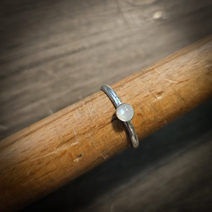Silver ring with a moonstone gemstone on a wooden stick against a blurred background