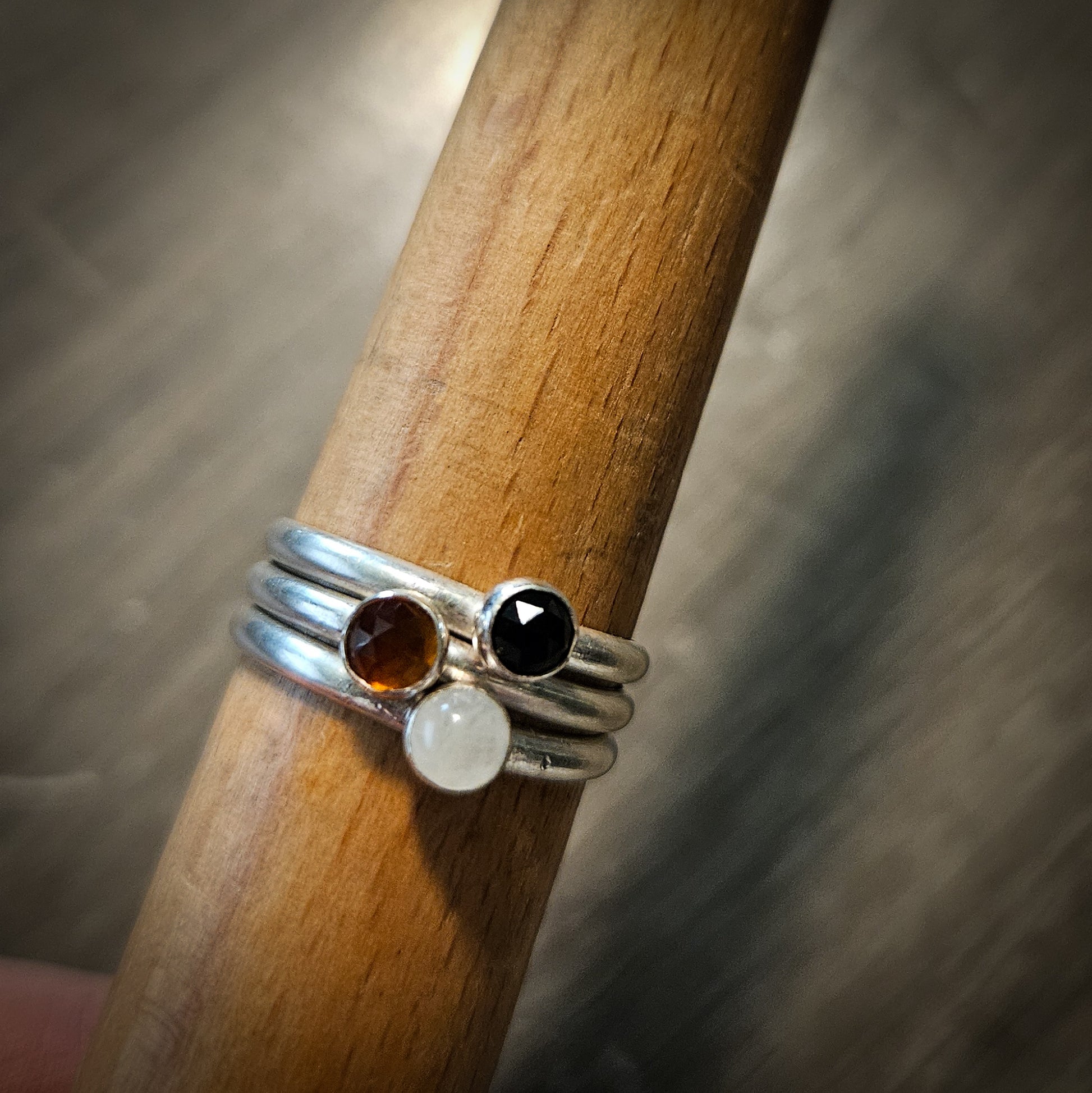 Three silver rings with gemstones on a wooden stick