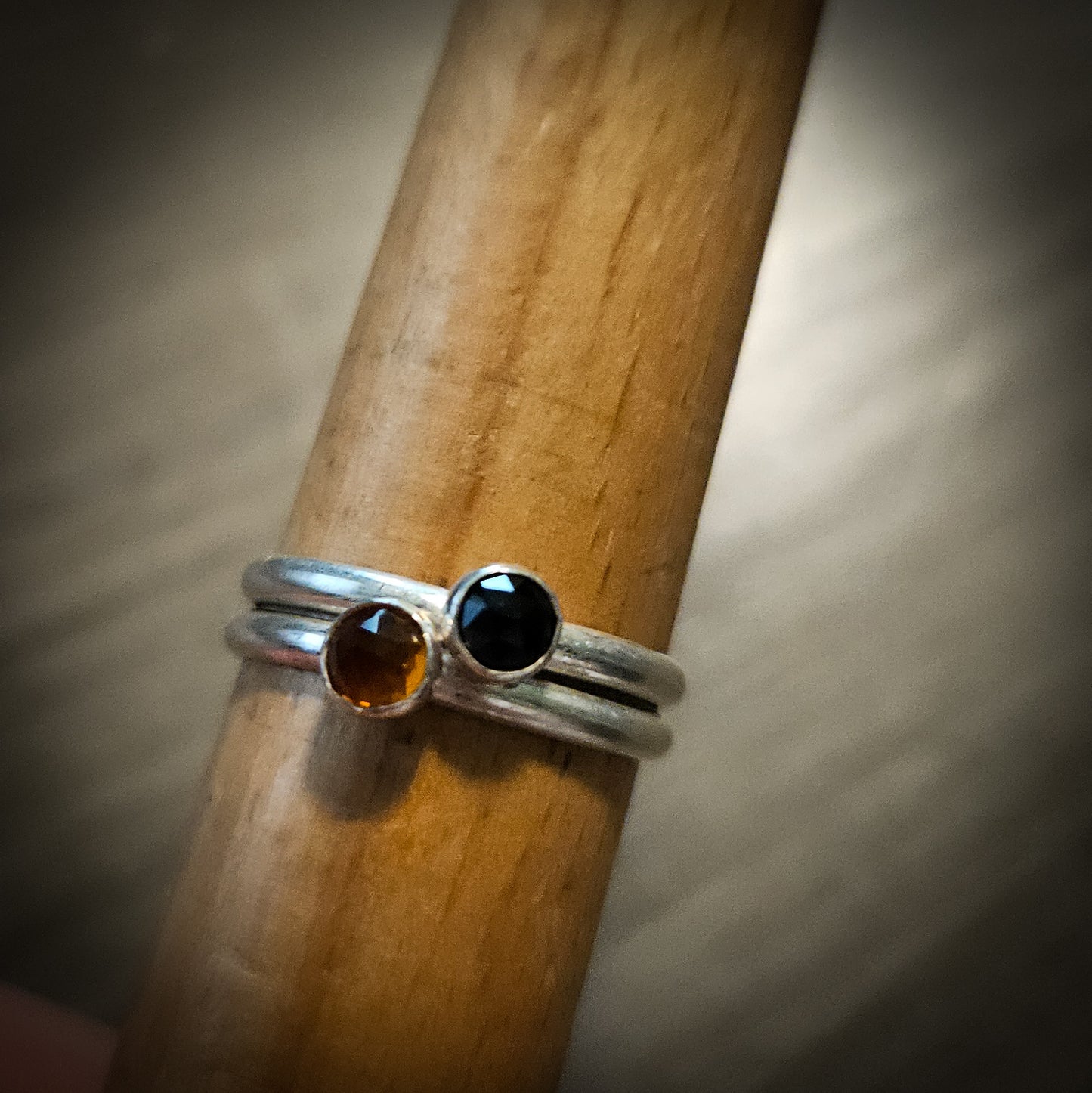 Two silver rings  – one with a black gemstone and one with an orange gemstone – on a wooden stick