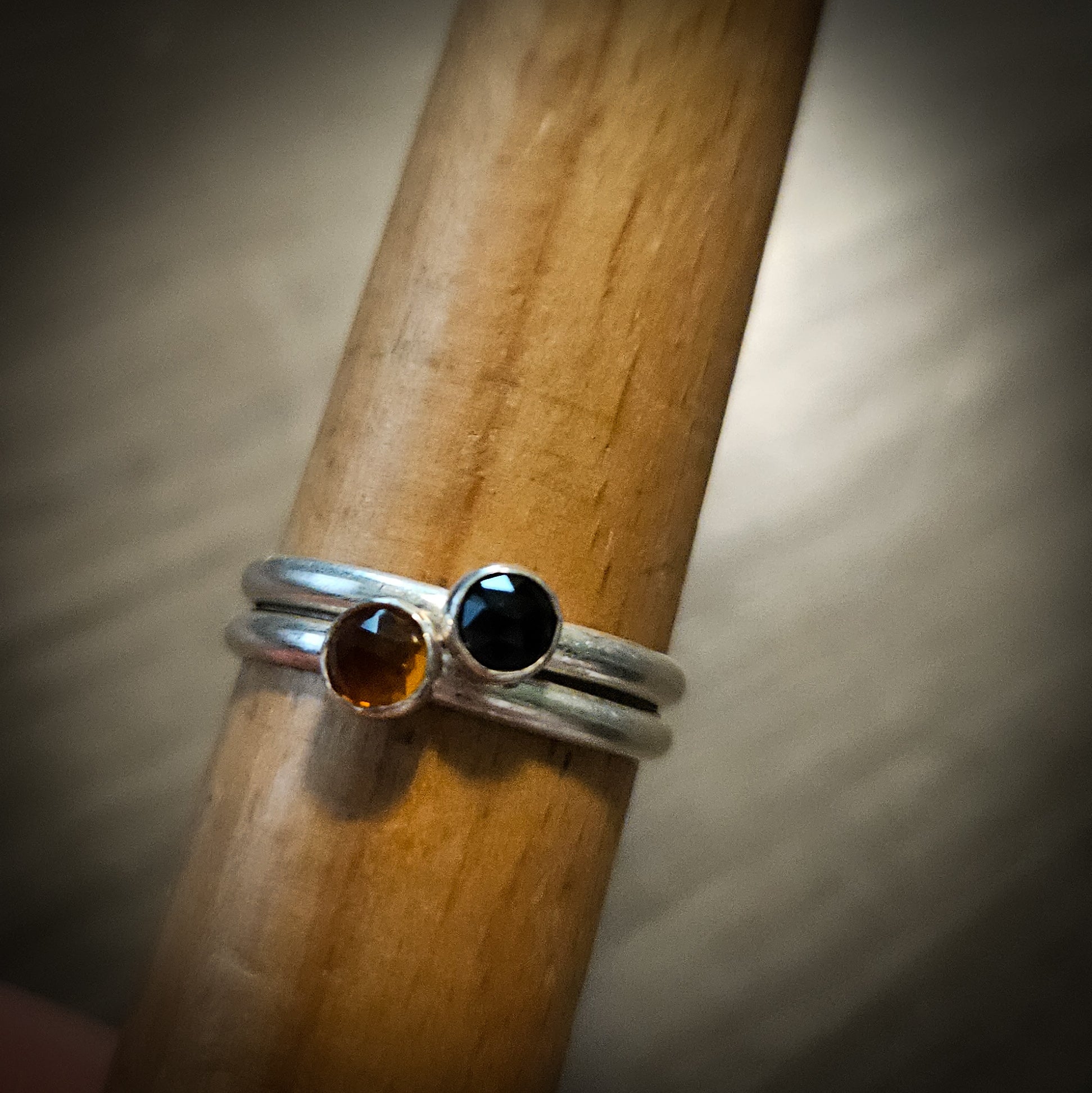 Two silver rings  – one with a black gemstone and one with an orange gemstone – on a wooden stick