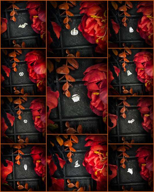 A collage of small sterling silver and brass Halloween-themed charms or pendants displayed on a dark grid background, surrounded by red flowers and autumn leaves. The charms include a witch hat, a cauldron, a skull, a pumpkin, a ghost, a bat, and a coffin.