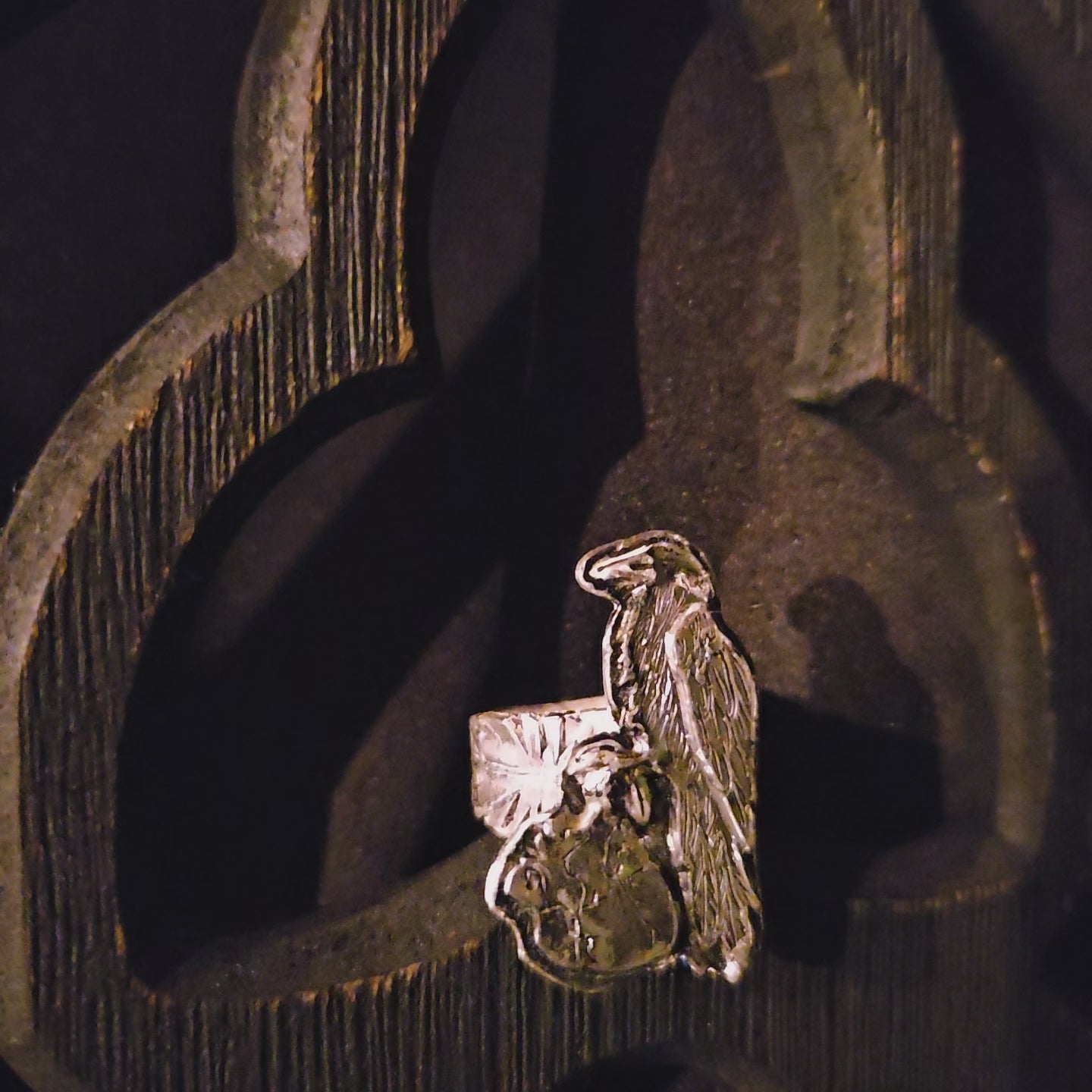 Sterling silver raven and human heart ring with a feather band on a dark wood background