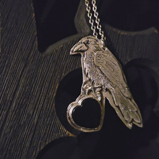 Sterling silver bird pendant with black heart stone on a chain against a dark wooden background