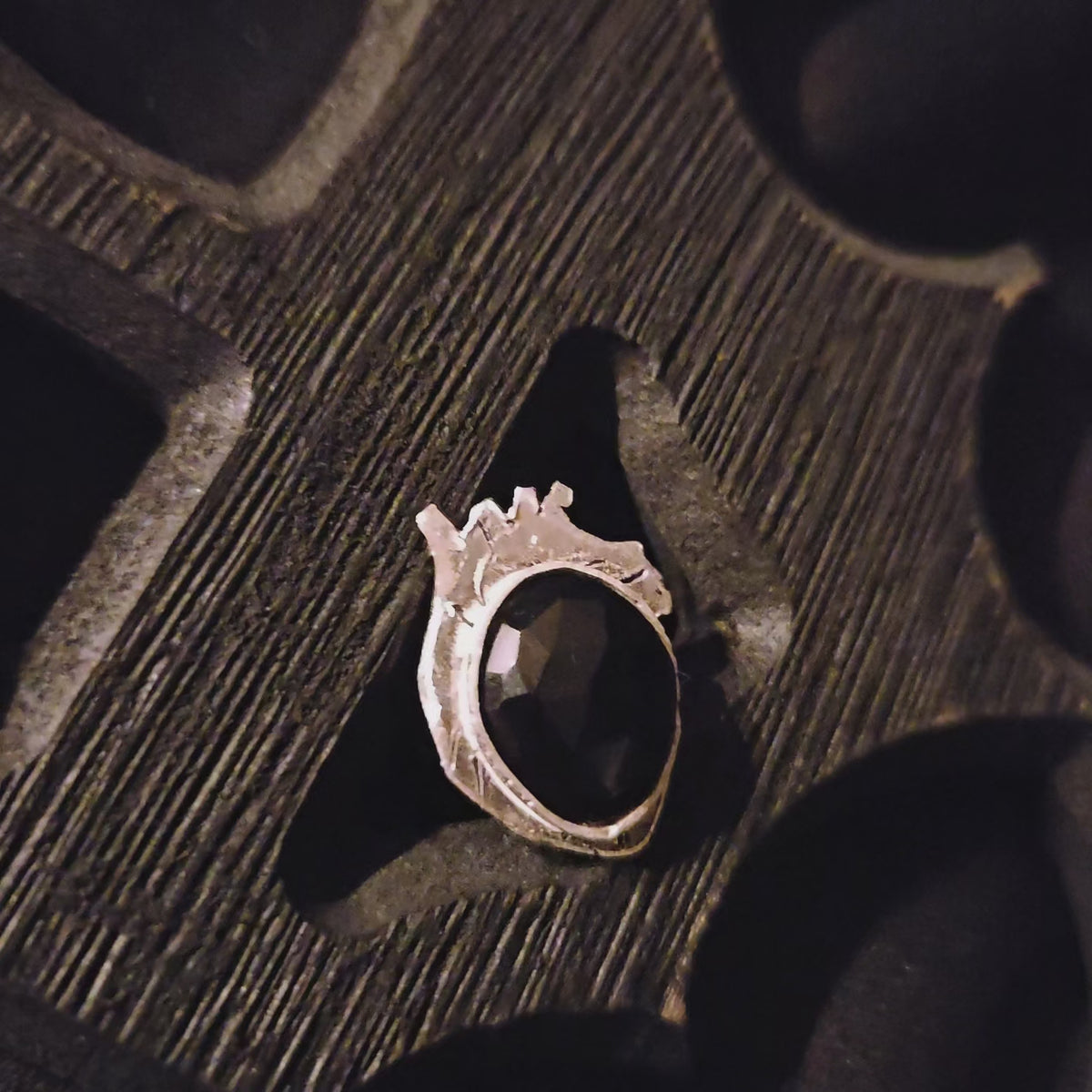 Silver ring with a black stone set on a heart shaped base displayed a wooden surface