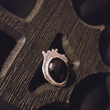 Silver ring with a black stone set on a heart shaped base displayed a wooden surface