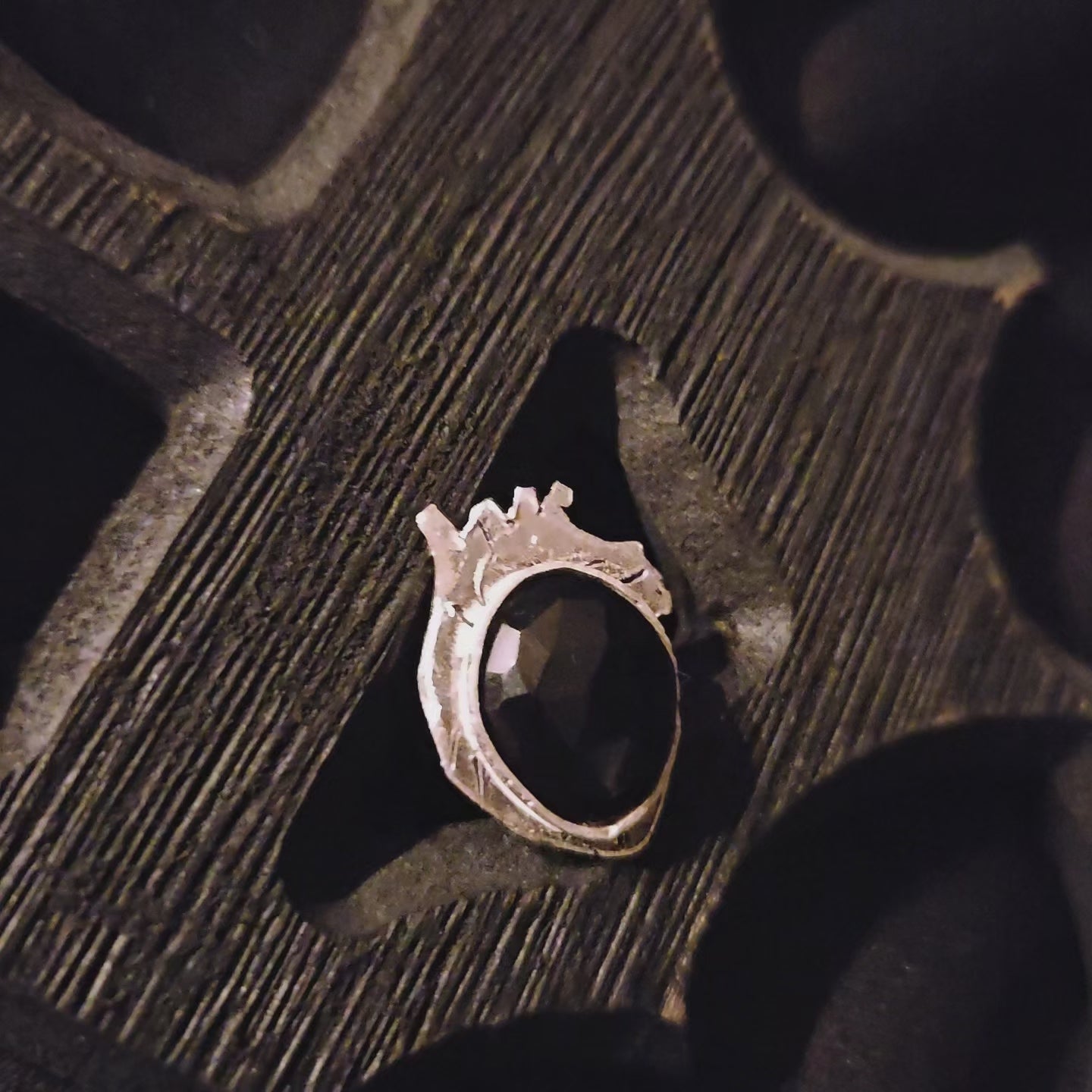Silver ring with a black stone set on a heart shaped base displayed a wooden surface