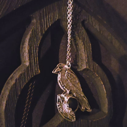 Silver pendant with a bird design and dark gemstone on a black background